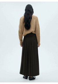 Hnědý pletený svetr doplněný dlouhou tmavou kostkovanou skládací sukní. Tento outfit má volný střih a texturovaný materiál.