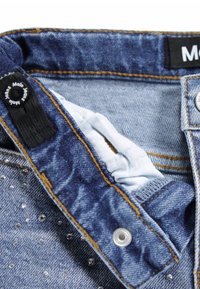 Jean en denim avec un intérieur bleu clair, un extérieur bleu sombre, orné de strass transparents et de coutures orange.