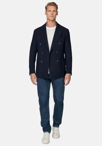 Granatowa, dwurzędowa marynarka z teksturowanej tkaniny, z dwoma kieszeniami, noszona na białej koszuli i niebieskich dżinsach z białymi sneakersami.
