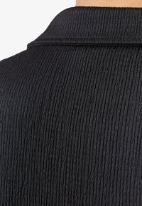 Κοντινό πλάνο μαύρου υφάσματος με κάθετο ραβδωτό μοτίβο και διπλωμένη άκρη γιακά.