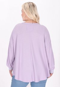 Lys lilla langærmet top med tekstureret stof, drop shoulder-design og ribbekanter. Bagsiden har en subtil nakkepatch-detalje.