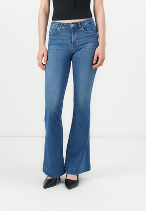 Jeans in denim blu a gamba svasata con lavaggio medio, design a cinque tasche e cuciture a contrasto. Abbinati a scarpe con tacco a punta nere.