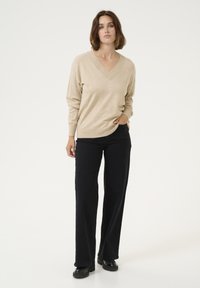 Pulover bej cu decolteu în V, dintr-un material moale, combinat cu pantaloni negri cu croi larg. Ținuta are o ajustare relaxată și un design minimalist.