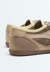 Paire de baskets beige en daim et mesh avec bordure beige et semelles marron, vues en angle arrière sur fond blanc.