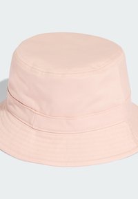Světle růžový klobouk s kšiltem vyrobený z hladké tkaniny, který má zaoblenou korunu a široký kšilt s jemným texturovaným detailem.