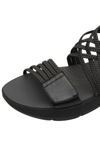 Czarne sandały z płaską podeszwą, plecionymi syntetycznymi paskami i fakturowaną wkładką. Wyściełany pasek zapewnia komfort na podbiciu.