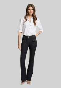 Jeans a zampa di elefante in denim blu scuro con due tasche frontali e bottoni decorativi, abbinati a una camicia bianca con bottoni caratterizzata da piccoli pois.