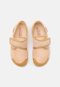 Persikofärgade nät-skor med ett beige elastiskt band, rund tå och en mjuk, texturerad sula. Märkesskylten synlig inuti skon.