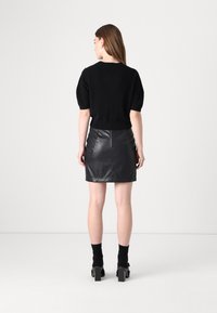 Svart strikket topp med korte ermer og tettsittende midje, kombinert med et svart skinn mini-skjørt. Kloss-helede sko fullfører antrekket.