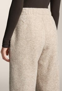 Svetlo bež mehke hlače iz teksturirane tkanine, z visokim pasom in ohlapnim krojem, s šivanimi detajli na pasu.