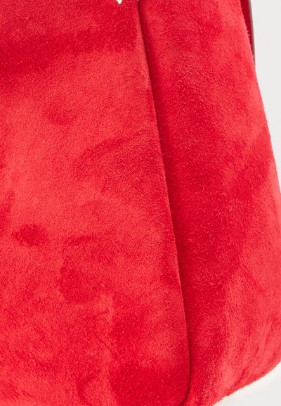 Κοντινή λήψη από ζωηρό κόκκινο ύφασμα από σουέντ με ορατή μαλακή υφή και ραφή σε μία πλευρά.