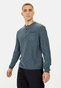 Langärmliges Henley-Shirt in Blau mit horizontalen Streifen, ausgestattet mit einer Knopfleiste und einer aufgesetzten Tasche auf der linken Brust. Texturiertes Material.