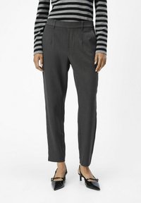 Dark gray tailored trousers with a smooth texture and side pockets, paired with black pointed-toe heels and a black-and-gray striped top.