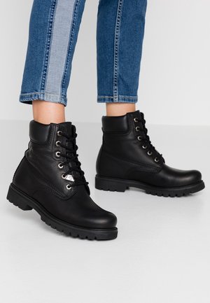 Person wearing black leather lace-up ankle boots and cropped blue jeans with a light denim stripe down the side.