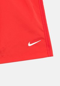 Røde treningsshorts laget av glatt, lett materiale. Har en hvit Nike-logo og sydd dekorasjon nær kanten.