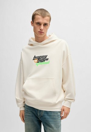 Haut à capuche couleur crème en tissu doux, doté d'une poche avant et d'un texte graphique en noir et vert. Coupe décontractée avec une capuche à cordon.