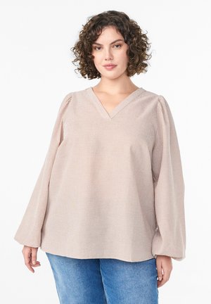 Vaaleanpunaista, teksturoitua puseroa, jossa on V-kaula-aukko ja puffatut pitkät hihat. Pusero on löysästi istuva ja siinä on pilkkukuosi, yhdistettynä sinisiin farkkuihin.