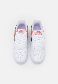 Vita Nike Air Force 1-sneakers med svart swoosh, orange detaljer, rund tå, perforerat ovandel och snörning. Mjuk textilfoder.
