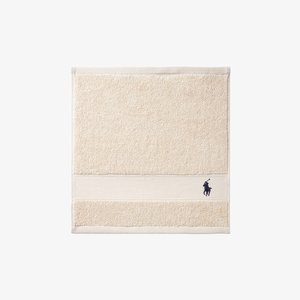 Beige terry cloth towel with a textured surface and a smooth stripe. Embroidered dark blue logo of a horseman with a mallet at the bottom.