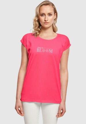 Pink short-sleeve t-shirt with a round neckline and “time to BLOOM” text printed in white, paired with white pants.
