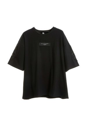 Camiseta negra oversize con una pequeña etiqueta rectangular en el pecho y un bordado negro parecido a plumas en ambas mangas.