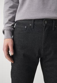 Jeans negre din denim cu un design ajustat, stil cu cinci buzunare și accente de hardware argintie. Materialul are o textură subtilă și un luciu.