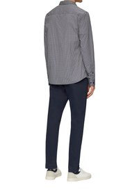 Overhemd met knopen in een marineblauw-wit houndstoothpatroon, geweven stof; gecombineerd met donkere broeken en witte sneakers. Zichtbare kraag en manchetten.