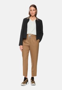 Black jacket with leopard-print collar, white top, tan tapered pants, and animal-print sneakers. Features elastic waistband and drawstring.