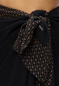 Μαύρο και καφέ ύφασμα με σχέδιο δεμένο σε κόμπο πάνω σε μαύρα ρούχα με μια μικρή μεταλλική καρφίτσα "BOSS" προσαρτημένη.