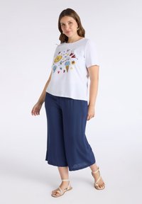 Top blanco de manga corta con un estampado colorido de temática veraniega. Combinado con culottes azul marino y sandalias beige. Tejido suave, corte relajado.