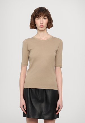 Beige kortærmet top med rund halsudskæring. Stoffet er glat, tætsiddende og kombineret med en sort lædernederdel, hvilket skaber kontrast i tekstur.