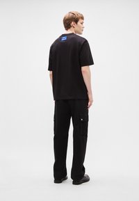 Μαύρη βαμβακερή μπλούζα με στρογγυλή λαιμόκοψη και κοντά μανίκια, με μπλε ταμπελάκι στην πλάτη. Συνδυάζεται με μαύρες cargo παντελόνες και μαύρα παπούτσια.