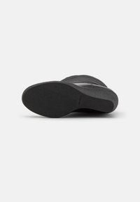 Botte noire à la cheville avec une semelle en caoutchouc texturée, une tige en cuir lisse et des détails de couture subtils. Présente un bout arrondi et un talon bas.