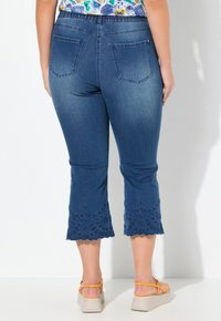 Pantalones capri de mezclilla con corte de altura media, que cuentan con un dobladillo festoneado bordado con patrones florales. Color azul oscuro, dos bolsillos en la parte trasera.