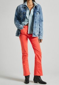 Chaqueta de mezclilla, camisa azul clara, pantalones de campana color coral y botas negras hasta el tobillo. La chaqueta tiene bolsillos; la camisa cuenta con botones.