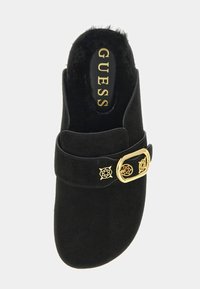 Chaussure à enfiler en daim noir avec doublure en fausse fourrure, détail boucle dorée et semelle intérieure de marque portant le nom "GUESS". Texture lisse.