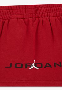 Κόκκινα βαμβακερά σορτς με ελαστική μέση, μαύρο κείμενο "JORDAN" και λευκό λογότυπο Jumpman τυπωμένα στο κάτω αριστερό μέρος.
