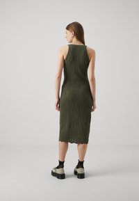 Strikket midikjole i olivengrønn, med ribbet tekstur og sittende silhuett. Designet med scoop-back og bølget hem-detalj.