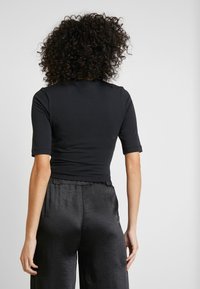 T-shirt noir cropped à manches courtes, fabriqué dans un tissu lisse, associé à un pantalon large en satin noir avec un subtil éclat.