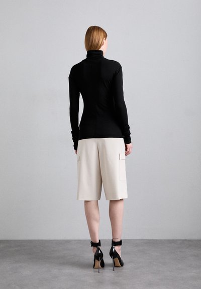 Musta pesupaita yhdistettynä beigen värisiin polvipituisii cargo-housuihin. Mustat korkokengät erottuvilla nilkkaremmillä. Sileä pinta, tiukka siluetti.