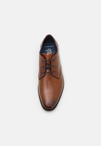 Braune Lederlackschuhe mit glatter Oberfläche, spitzem Zehenbereich und schwarzen Schnürsenkeln. Innen befindet sich eine blaue gepolsterte Einlage mit dem Aufdruck "Comfort Wide".