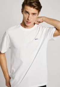 Vits bomull t-shirt med rund halsringning och korta ärmar. Har en liten mörkblå logotyp på vänster bröstområde. Slät textur.