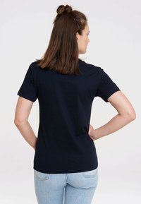 Navy blue cotton t-shirt with short sleeves and a crew neckline, viewed from the back, paired with light blue jeans.