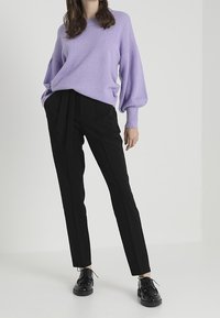 Světle fialový svetr s volným pletením a balónovými rukávy, kombinovaný s dobře padnoucími černými kalhotami s uvázaným pasem a elegantními černými botami.