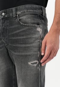 Čierne džíny z denimového materiálu s priliehavým strihom, jemným udalšovaním, opotrebovanými detailmi na stehne a gombíkovým zapínaním v páse.