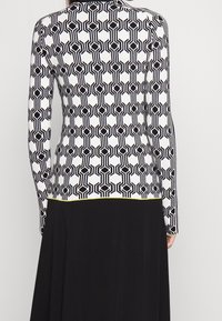 Top de manga larga con un patrón geométrico en blanco y negro y ribete amarillo en la parte inferior. Confeccionado con una tela texturizada y elástica.