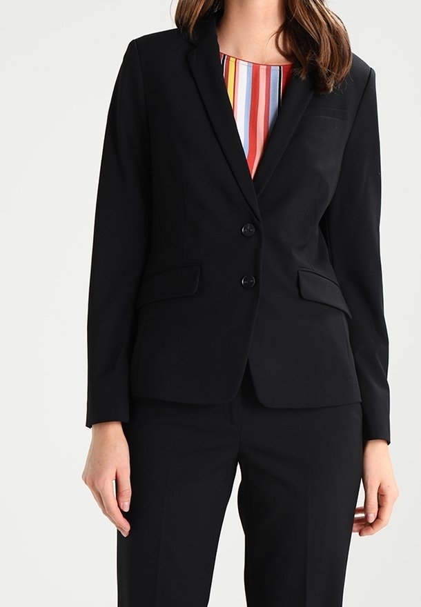 Femme portant un blazer noir ajusté à deux boutons sur un chemisier multicolore à rayures verticales, associé à un pantalon noir assorti.
