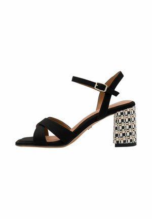 Sort åben tå-sandal med krydsede remme, ankellukke og blokhæl med et hvidt og sort vævet mønster.