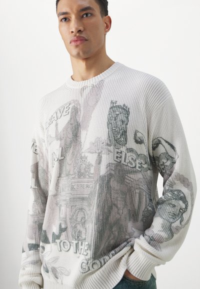 Hellbeige gestrickter Pullover mit schwarzen Grafiken, die verschiedene historische Figuren und Text zeigen. Rippkragen und -manschetten.