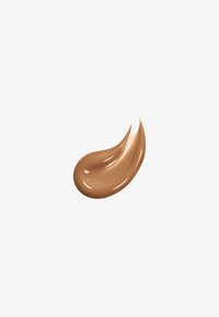 Slick, bronzfärgad kosmetisk kräm med en glittrig finish, formad som en liten, böjd klump. Konsistensen verkar krämig och glansig.